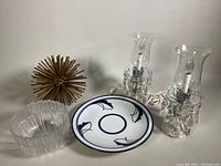 Lot showing two clear glass hurricane-style table lamps with crystal hanging accents and glass chimneys, brass Sputnik style decor piece, Dansk decorative plate with blue floral design, small finish flaw visible on plate.