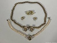 Photo showing Miriam Haskell gold-tone twisted rope chain necklace and pearl necklace with rhinestone clasp, along with a gold-tone bird brooch and matching earrings.