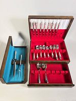 Full view of two wooden cases with silverware inside, showing red felt and white satin lining for main case, blue felt lining for carving case, and visible wear on wood finish.