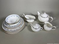 Full set with stacked plates and bowls, showing Memory Lane pattern blue floral and gold trim, and Everlasting pattern teapot, sugar bowl, creamer in white with silver trim.