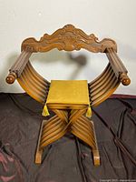 Front view of wooden Savonarola style chair with yellow seat pad and carved crest rail.