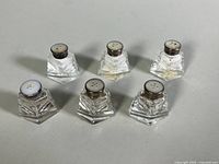 Set of six small salt and pepper shakers arranged on a surface, showing tops with sterling silver caps and faceted clear glass bodies.