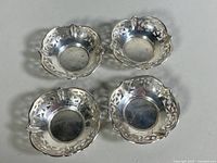 Top view of four sterling silver trinket dishes arranged in a square, showing decorative pierced edges and polished finish.