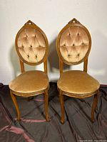Front view of two vintage chairs side by side with tufted oval backs, carved wooden frames, and fabric seats