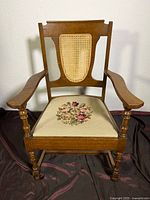 Front view of vintage wooden armchair showing the cane backrest and needlepoint floral seat cover.