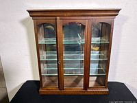 Front view of wood display case showing three glass shelves and mirrored back with glass door panels.
