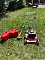 Full view of lawn mower, string trimmer and two gas cans on grass
