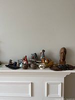 Wide view of assortment on mantel showing ceramics, pottery, and wooden decor items, including figurines and carved combs