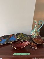 Photo showing colorful swirling decorative plates in black and red leaf-shaped plates along with the tall floral jug.