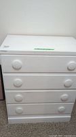 Front view of the white dresser showing four drawers with round knobs