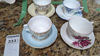 Photo showing four fine china teacups each paired with a saucer, decorated in various floral and gold accents.