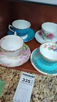 Four fine china teacups and saucers displayed with varied floral and blue designs.