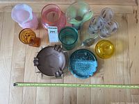 Top-down view of various glass and ceramic vases, ashtrays, and decorative items arranged on a wooden surface with measuring tape for scale.