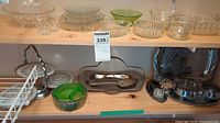 View of glass serveware on top shelf including clear and green glass bowls and plates, two-tier metal stand, and metal trays on bottom shelf.