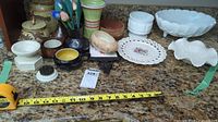 Full view of all items arrayed on a countertop showing milk glass bowls, pottery and ceramic canisters, and decorative pieces.