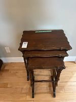 Three wooden nesting tables stacked showing carved edges and legs.