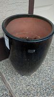 Showing one ceramic garden pot from top and side view, black glazed exterior, terracotta interior with soil inside