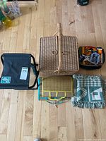Closed wicker picnic basket with cooler bag, woven mat, folded blankets and embroidery hoop around on wooden floor