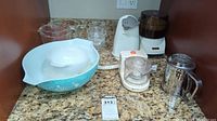 Full view of mix of Pyrex mixing bowls, measuring jugs, electric can opener, mini chopper, and electric juicer on kitchen counter.