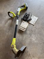 Full view of Ryobi 18V string trimmer/edger with battery, charger, and manuals on concrete floor.