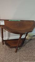 Front angle view of half-circle wooden side table showing top surface, legs, and lower shelf.