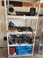 Plastic shelving stand loaded with assorted power tools, cords, and tarps visible on multiple shelves.