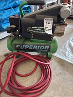 View of entire green Superior air compressor with attached red hose and identification label showing brand and model.