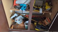 Photo showing a variety of tools, including circular saw, chainsaw, several hand saws and a metal miter saw in a garage shelf.