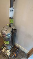 Hoover WindTunnel upright vacuum cleaner showing main body, hose, and accessories leaning against a wall.