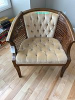 Full view of vintage wicker tub chair with beige tufted upholstery and wooden frame with woven wicker panel sides.