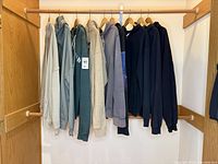 Nine hooded sweatshirts hanging on wooden hangers in closet