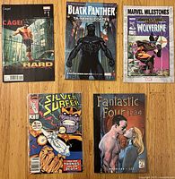 Five assorted comics laid flat: Cage! Hard #1, Black Panther Book One, Marvel Milestones Wolverine, The Silver Surfer Thanos cover, Fantastic Four 1234