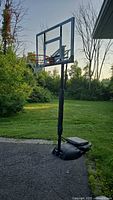 Full view of the portable basketball hoop outdoors on pavement, showing base, adjustable black pole, and clear backboard with red rim and white nylon net.