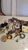 Wide view of assorted jewelry including chains, bead necklaces, bracelets, brooches, and pendants spread out on a white surface