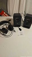 Full lot including Logitech speakers and black wired headset on a flat surface with white backdrop.