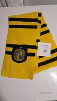 Yellow and black striped knitted scarf with Hufflepuff crest patch laid flat on white surface.
