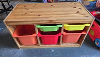 Front view of the wooden storage unit showing all five plastic bins in various colors inside the wooden frame.