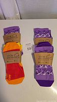 Top view of four pairs of women's socks on a white surface: three purple patterned pairs and one red/orange/yellow pair with paper labels.