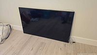 Front view of 55" Samsung TV leaning against wall with attached cable