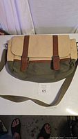 Front view of a two-tone canvas and leather shoulder bag with buckle straps and adjustable shoulder strap.