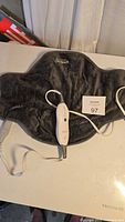Grey Sunbeam branded heating neck blanket laid flat with attached wired controller.