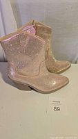 Side view of the pair of women's shiny boots, showing light pink/nude color and rhinestone cover, mid-height chunky heel