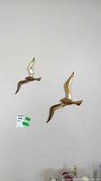 Both brass bird wall art pieces mounted together on wall, highlighting size difference and design.