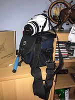 Photo showing white Pentax K-x DSLR camera with 18-55mm lens on black Optex shoulder bag, placed on wooden surface near other miscellaneous items.