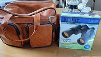 Vivitar binoculars box next to brown textured carrying case on table.
