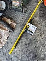 Yellow pole limb cutter and instruction manual lying on a garage floor.