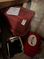 Red plastic storage bins stacked with one on the floor holding various items plus two coolers beside them