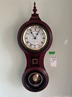 Full front view of the banjo style wall mounted clock, showing its overall shape and design including pendulum and finial.