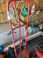 Front view of red metal moving dolly showing handle and base plate with rust and wear.