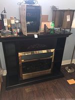 Dimplex electric fireplace insert within a black wooden surround. Surround features shelves and housing above the fireplace area with various items on top.